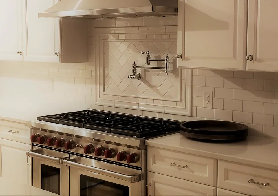 Framed herringbone tile backsplash installed by Plymouth Home, behind a professional range and pot filler